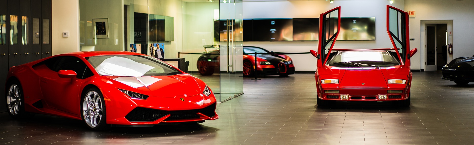 Luc van Bussel - Automotive Hospitality - 2 rode Ferrari's in een showroom waarvan 1 met de deuren omhoog open.
