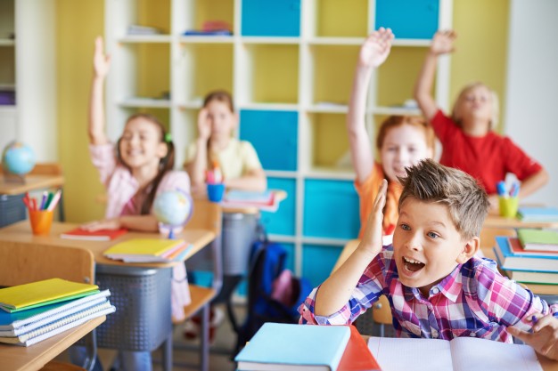 Luc van Bussel - School Hospitality - kinderen in de klas achter tafeltjes en steken hun handen omhoog
