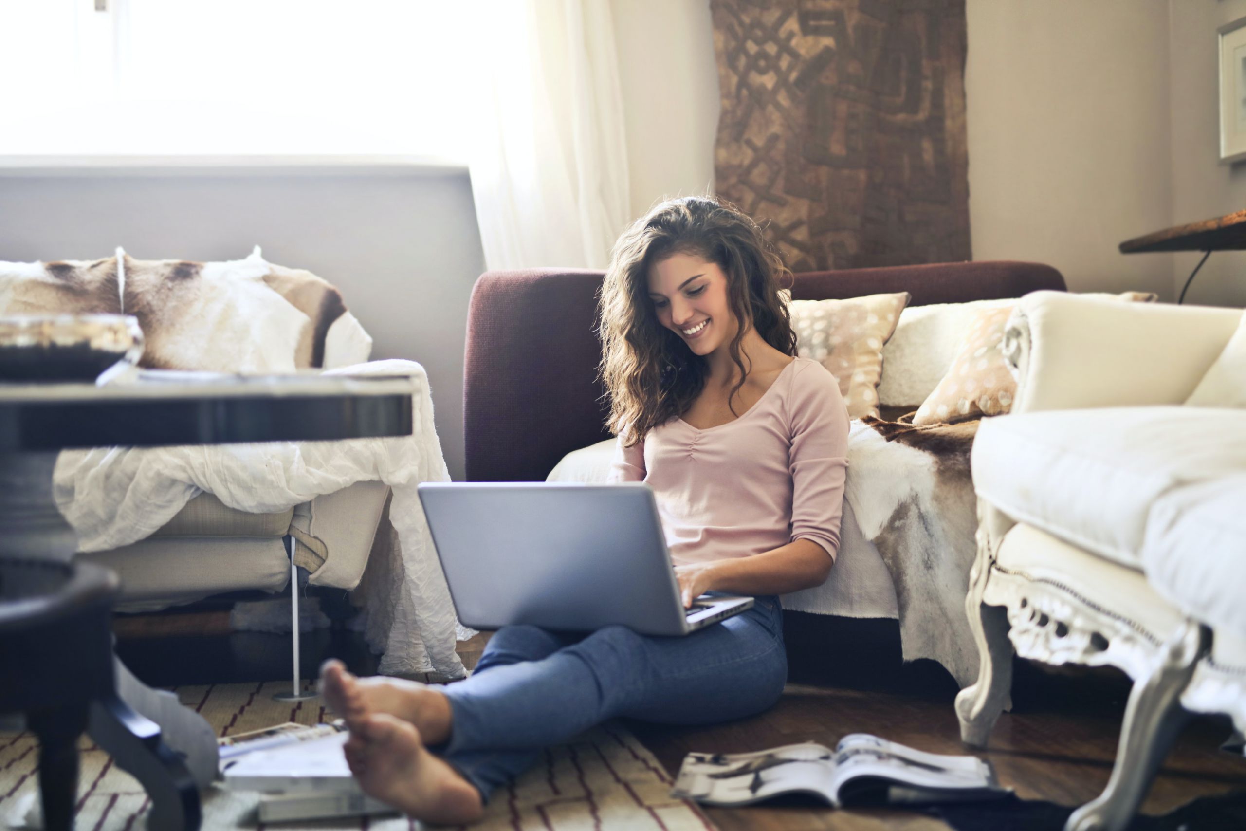 Luc van Bussel - Online Hospitality - Jonge dame zit voor de bank te werken op haar laptop in huiskamer.